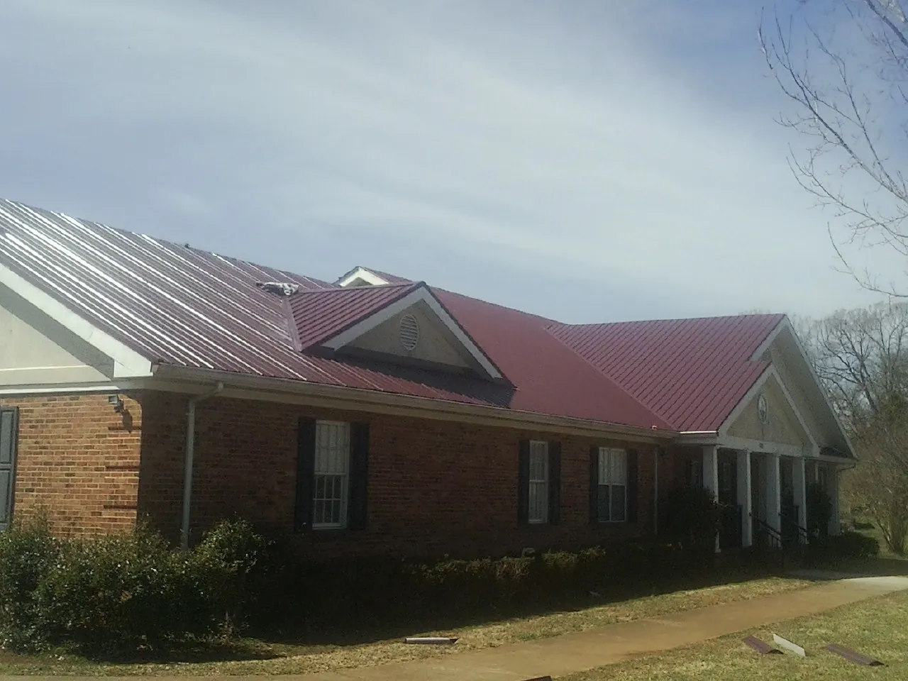 Red metal roof with gabled entries on a long brick building, from a Hail Damage Roof Repair job in Girard