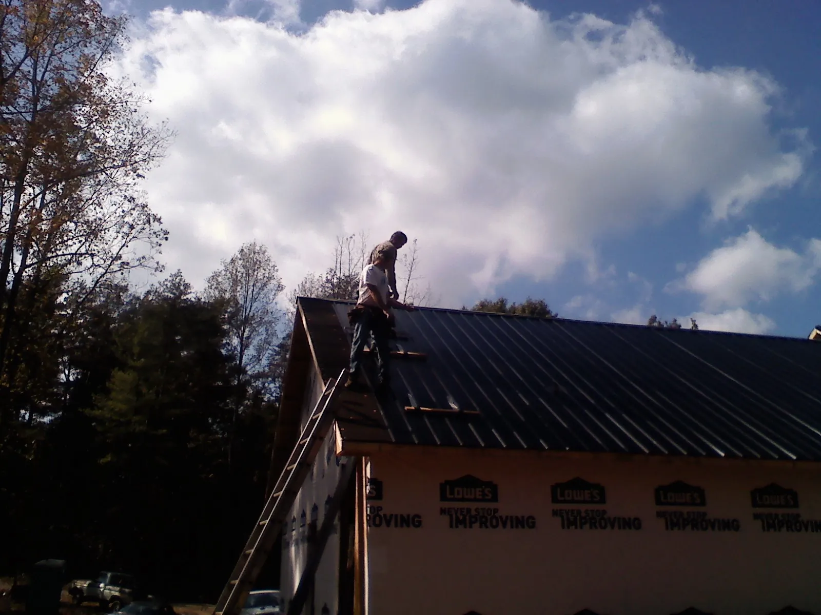 Roofer fastening dark metal panels high against a cloudy sky, from a Roof Inspection job in Girard
